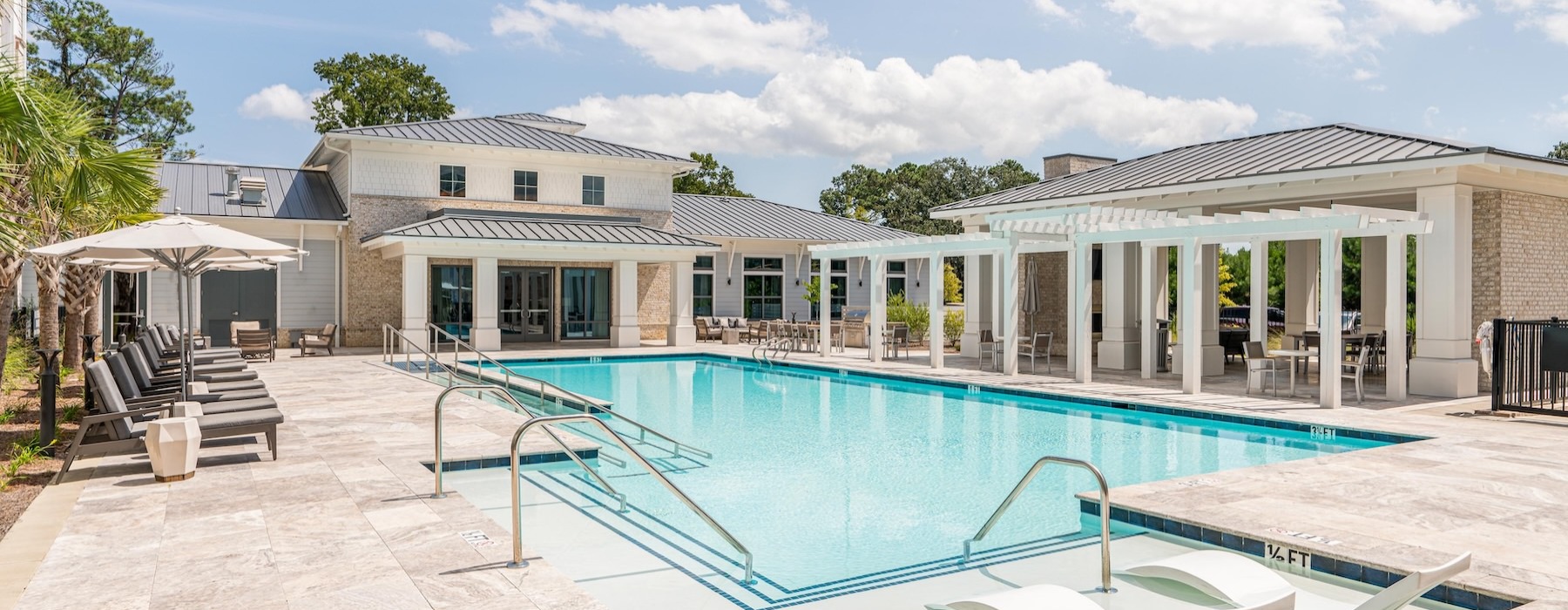 The pool area at Overture West Ashley senior living apartments in Charleston, SC, featuring lounge chairs and umbrellas.