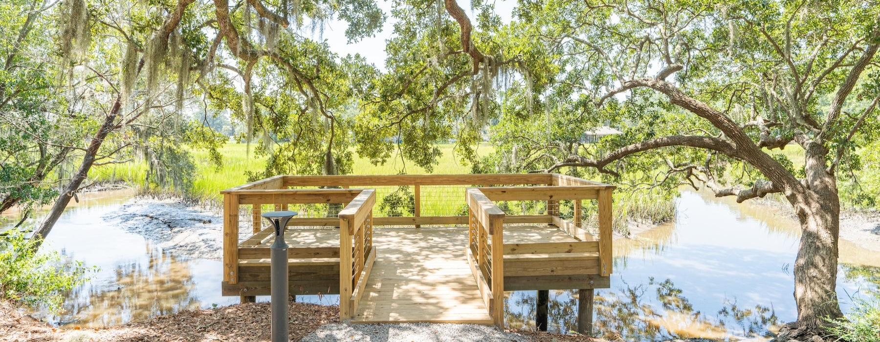A dock by the lagoon at Overture West Ashley senior living apartments in Charleston, SC, featuring overhanging trees.