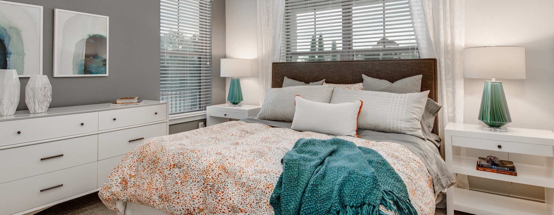 Model bedroom at Overture Stone Oak apartments in San Antonio, TX, featuring a bed, bedside table, dresser, and windows.
