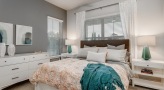 Model bedroom at Overture Stone Oak apartments in San Antonio, TX, featuring a bed, bedside table, dresser, and windows.