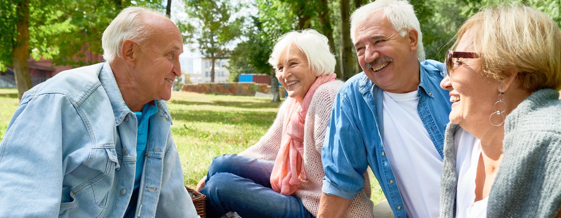 Residents sitting on the grass near Overture Plano senior living apartments in Plano, TX, featuring warm sunlight.