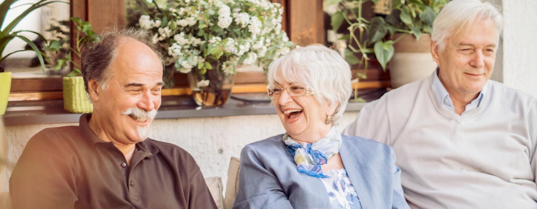 Residents sitting outside laughing at Overture Riverwalk senior living apartments in Riverside, CA, featuring warm sunlight.