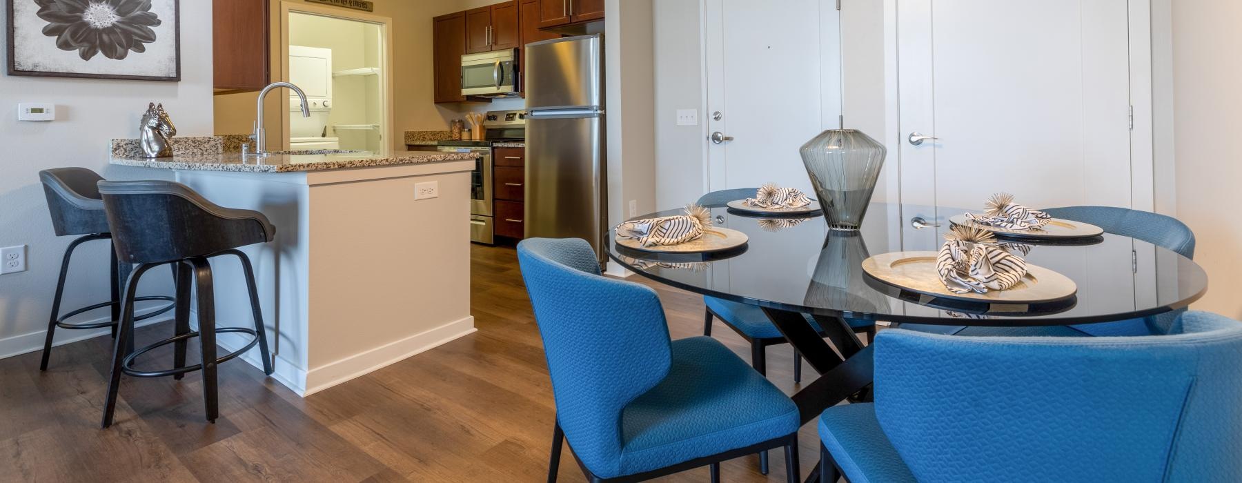 Model dining room and kitchen at Overture Central Park senior apartments in Denver, CO, featuring wood grain floor paneling.