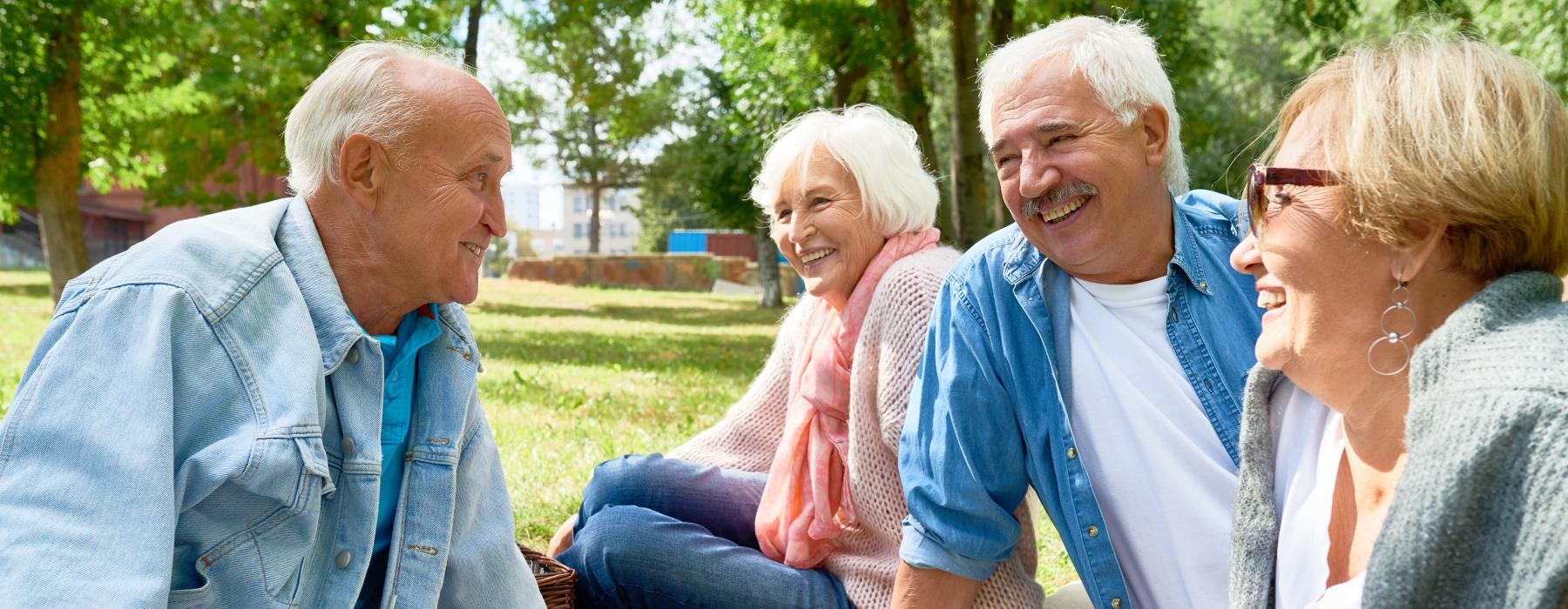 Residents sitting on the grass and smiling near Overture 9th + CO senior apartments in Denver, CO, featuring warm sunlight.
