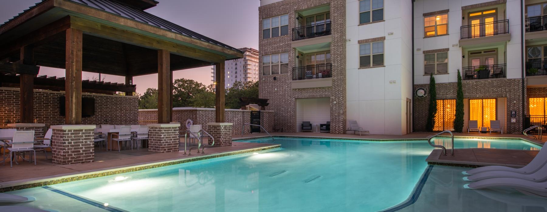 The pool area at Overture Flower Mound 55 plus apartments in Flower Mound, TX, featuring outdoor couches and a TV.