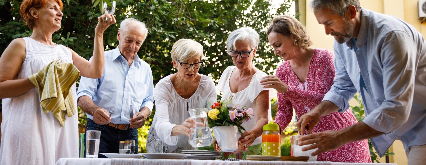 Residents standing outside around a table with flowers at Overture West Ashley senior living apartments in Charleston, SC.