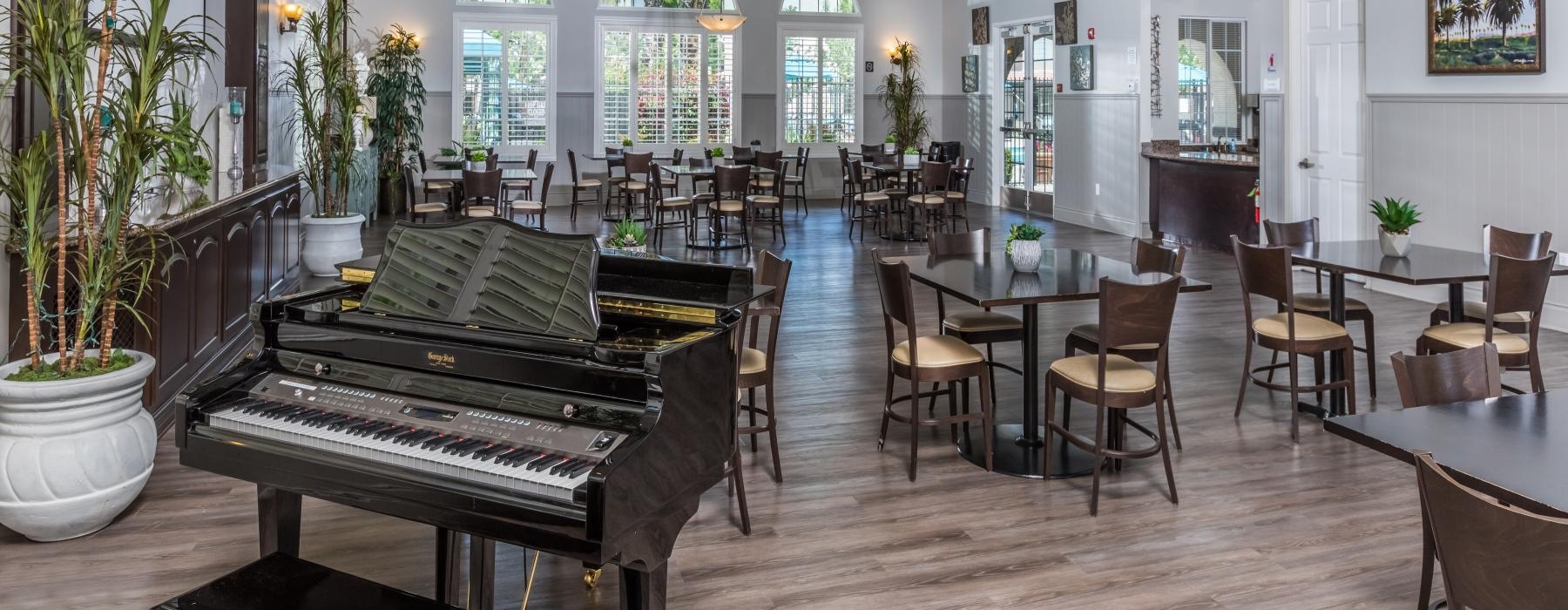 The resident lounge at Overture Riverwalk senior living apartments in Riverside, CA featuring a piano and tables with chairs.