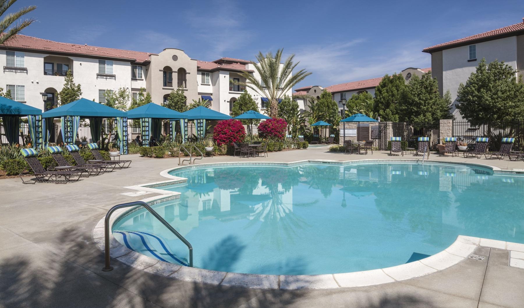 The pool area at Overture Riverwalk senior living apartments in Riverside, CA, featuring umbrellas and outdoor furniture.
