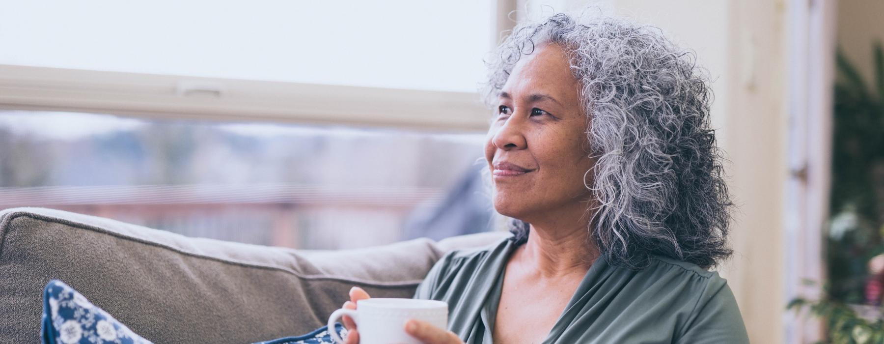 woman sitting on a couch next to a large window with a cup of tea in her hands