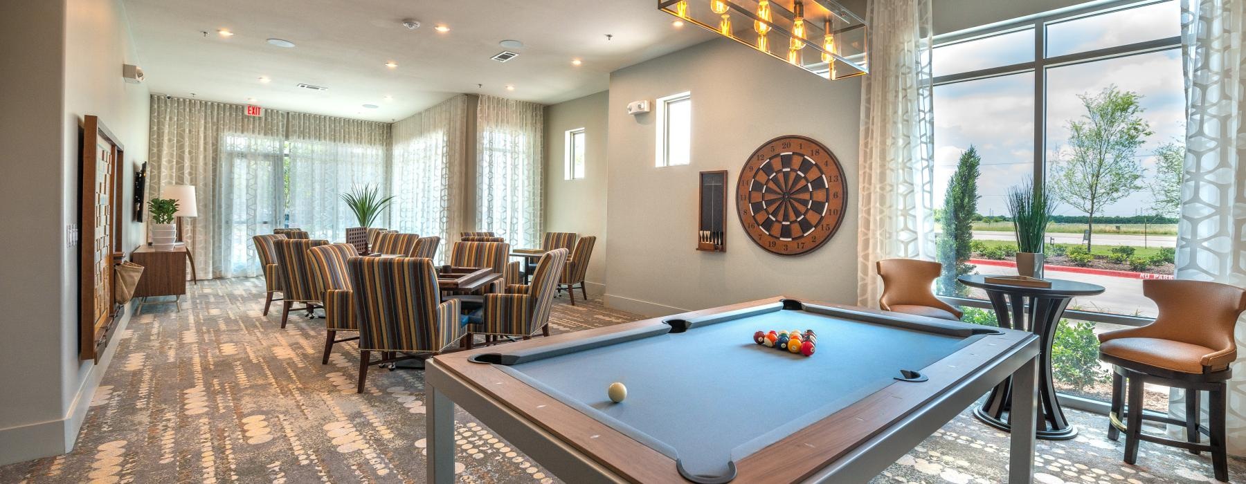 Resident lounge at Overture Plano senior living apartments in Plano, TX, featuring carpeted flooring and a billiards table.