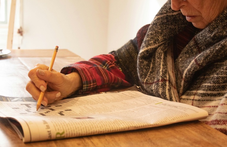 A resident doing a crossword at Overture Fair Ridge senior living apartments in Fairfax, VA, featuring natural lighting.