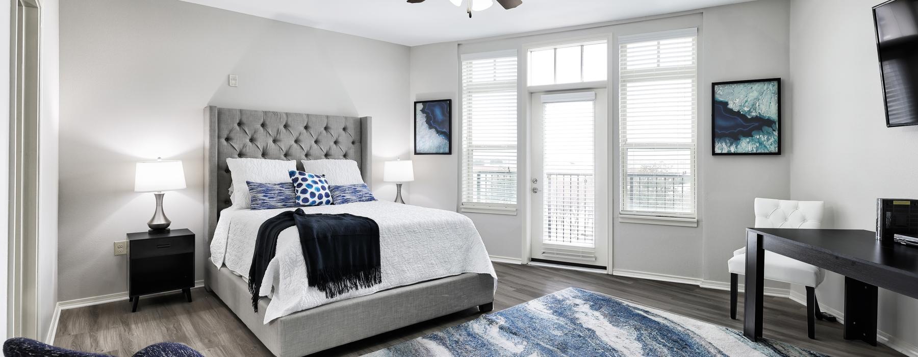  Model bedroom at Overture Ridgmar senior living apartments in Fort Worth, TX, featuring wood grain flooring and a balcony.