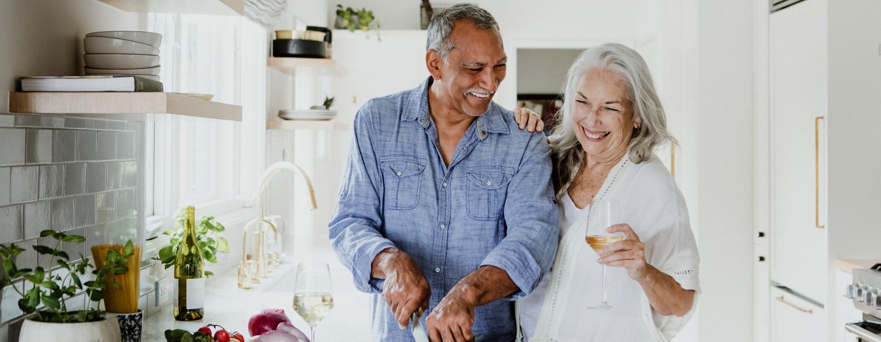 Man and woman cooking and laughing in a well lit kitchen 