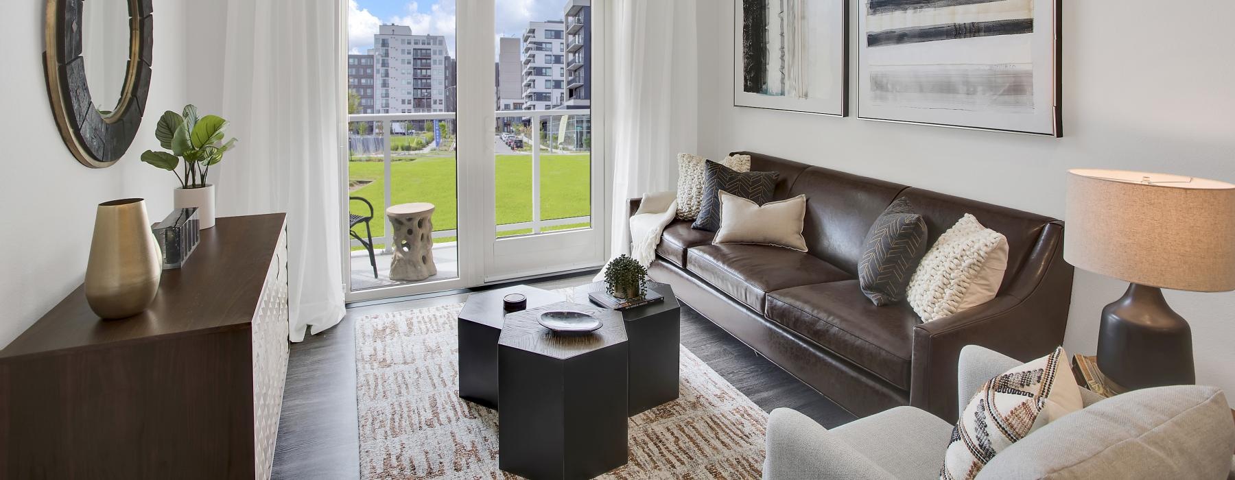 Model living room at Overture 9th + CO senior apartments in Denver, CO, featuring wood grain flooring and doors to the porch.