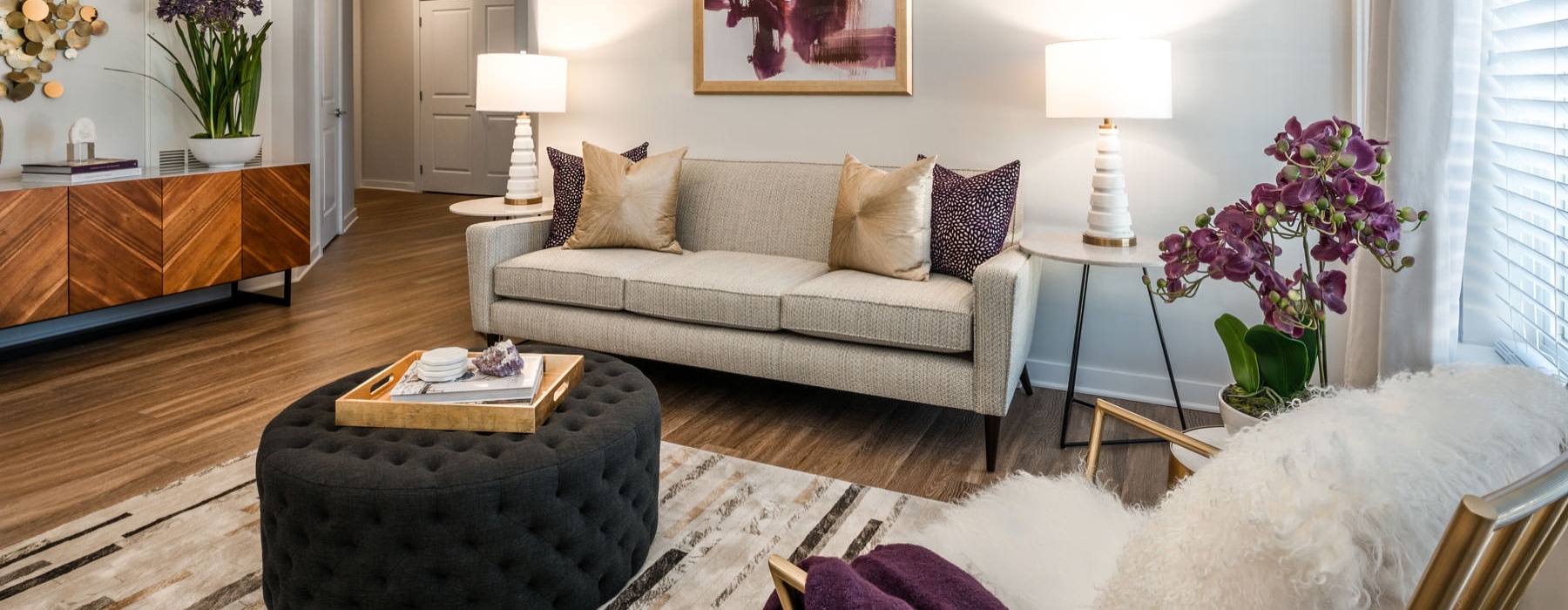 Model living room at Overture Fair Ridge senior living apartments in Fairfax, VA, featuring wood grain floor paneling.