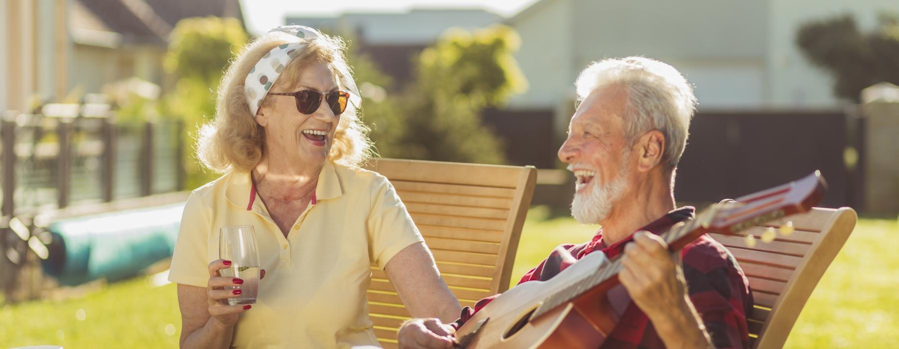 Two residents sitting outside with a guitar at Overture Riverwalk senior living apartments in Riverside, CA.