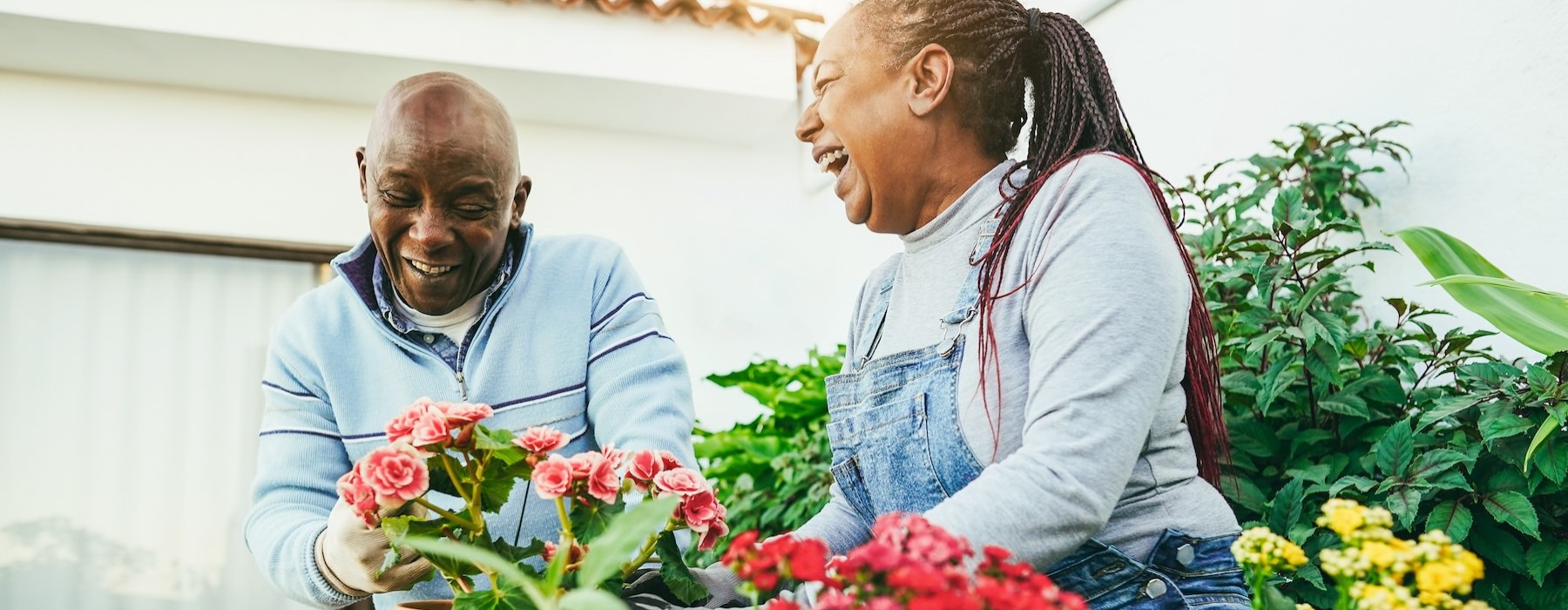 Two people outdoors laughing and gardening at Overture Stone Oak apartments in San Antonio, TX, featuring colorful flowers.