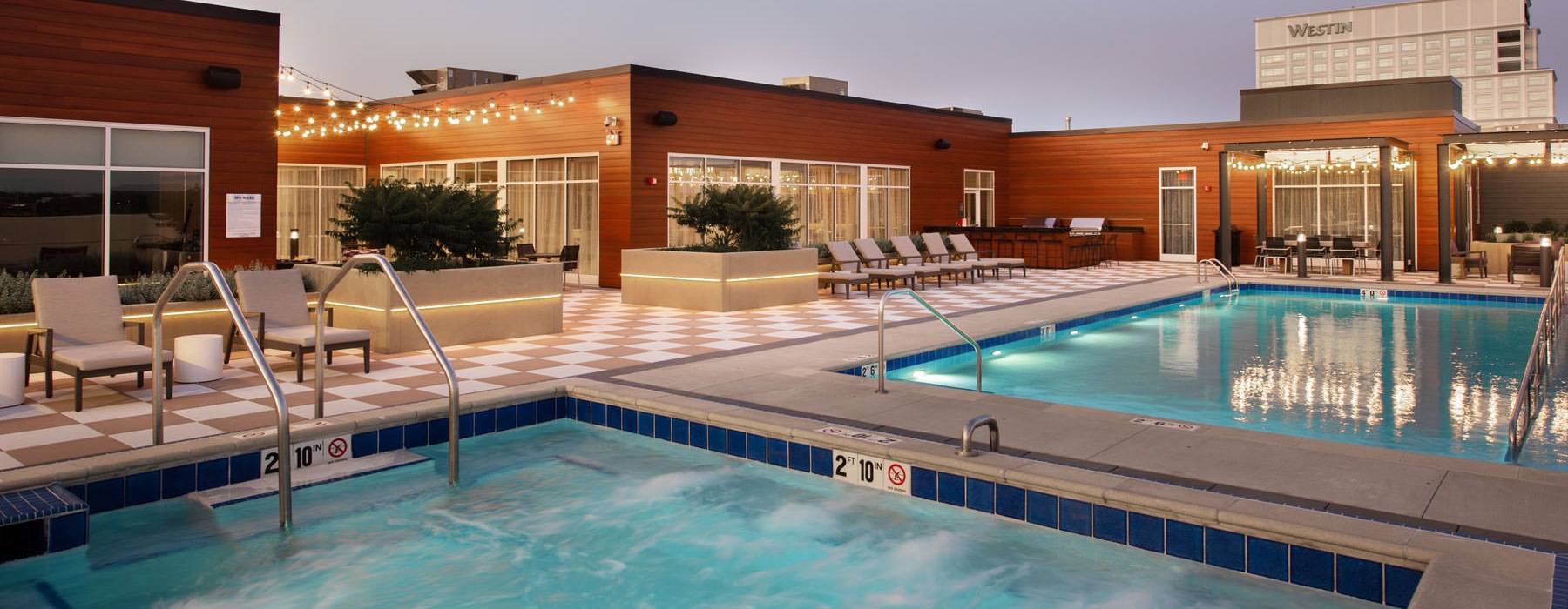 The pool area at Overture Yorktown 55 and older apartments in Lombard, IL, featuring lounge chairs and string lights.
