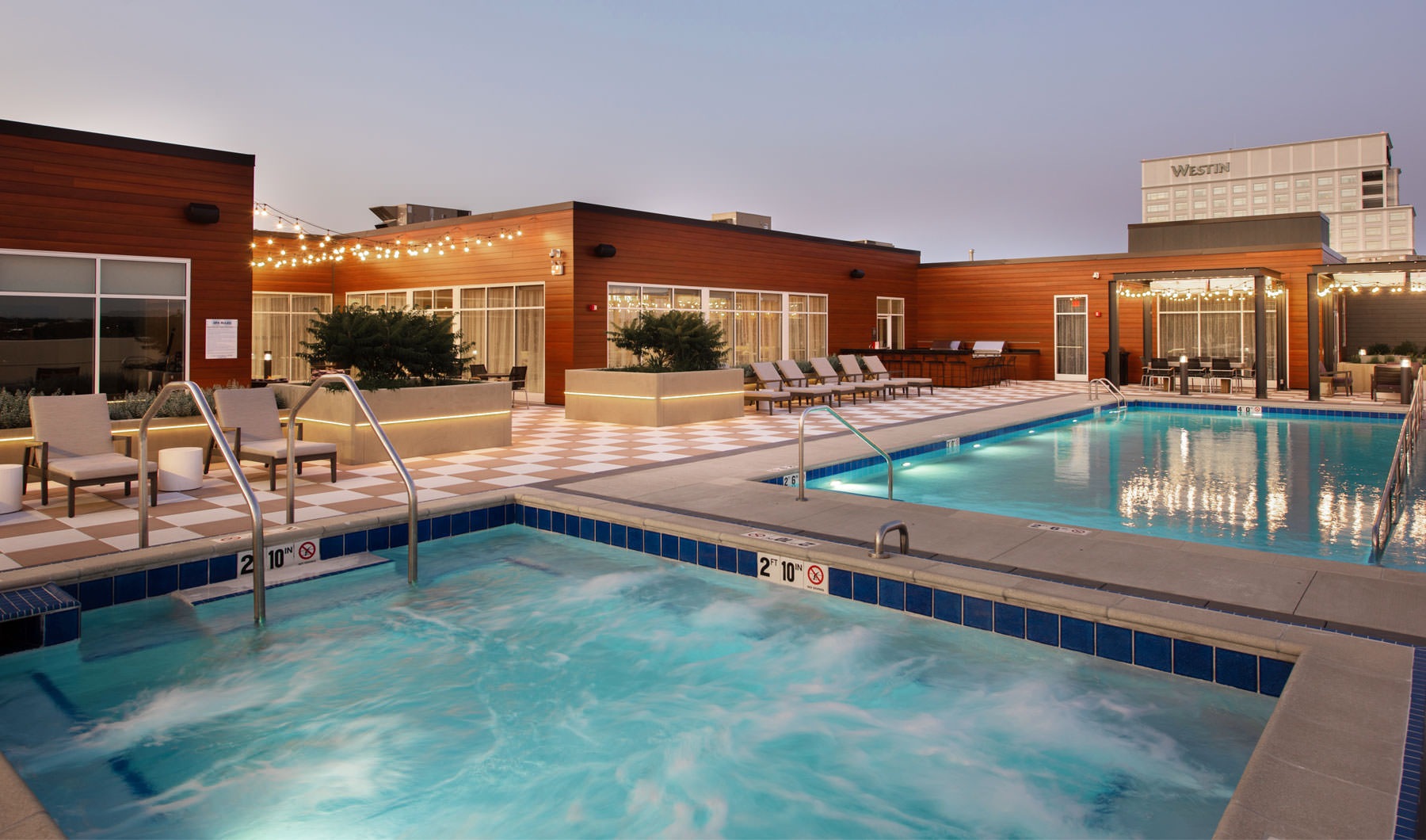 The pool area at Overture Yorktown 55 and older apartments in Lombard, IL, featuring lounge chairs and string lights.